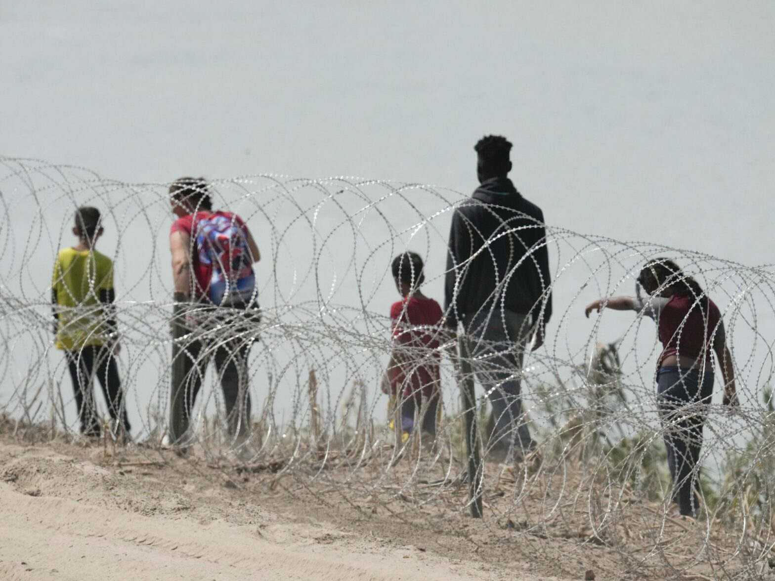 A group of migrants look for an opening in the concertina wire barrier south of Eagle Pass where a 1000-foot string of buoys has been placed in the river to deter crossing the Rio Grande River into Texas.