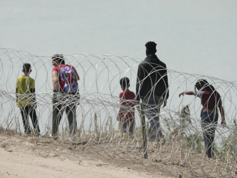 A group of migrants look for an opening in the concertina wire barrier south of Eagle Pass where a 1000-foot string of buoys has been placed in the river to deter crossing the Rio Grande River into Texas.