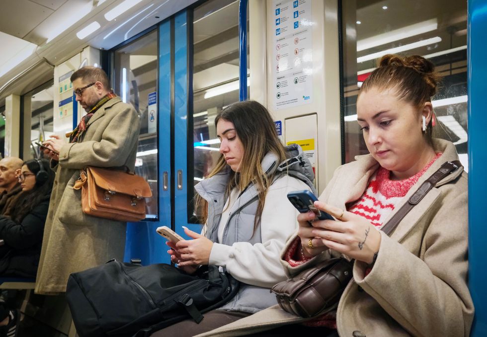 A group of people on a train are all on their phones with earbuds in.