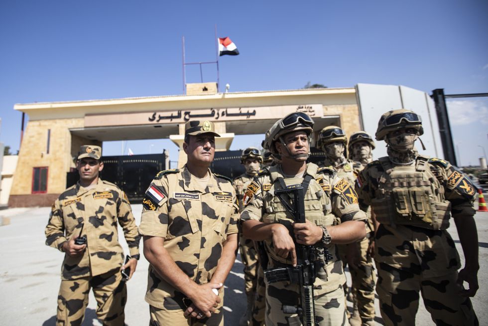 A group of soldiers stand in front of a sandstone border crossing