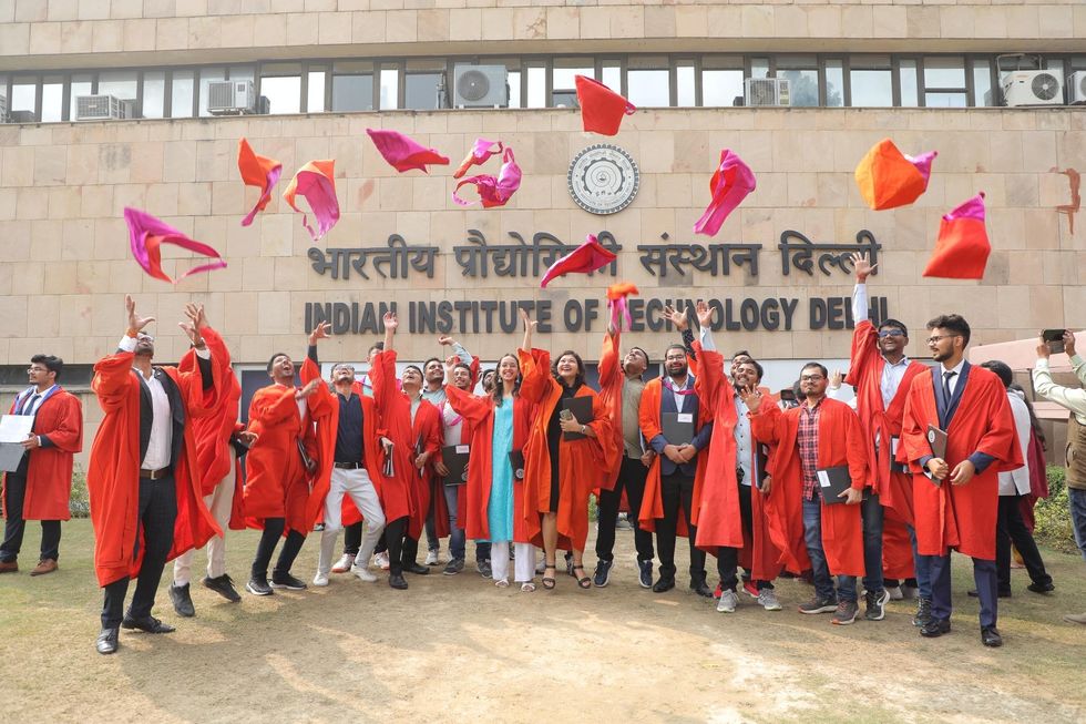 A group of young graduates in orange robes throwing des caps in the air, in front of the Indian Institute of Technology Campus