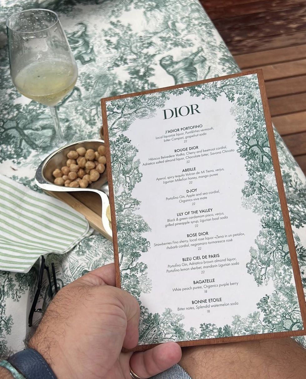 A hand holds a Dior menu above the decorate table of a terrace.