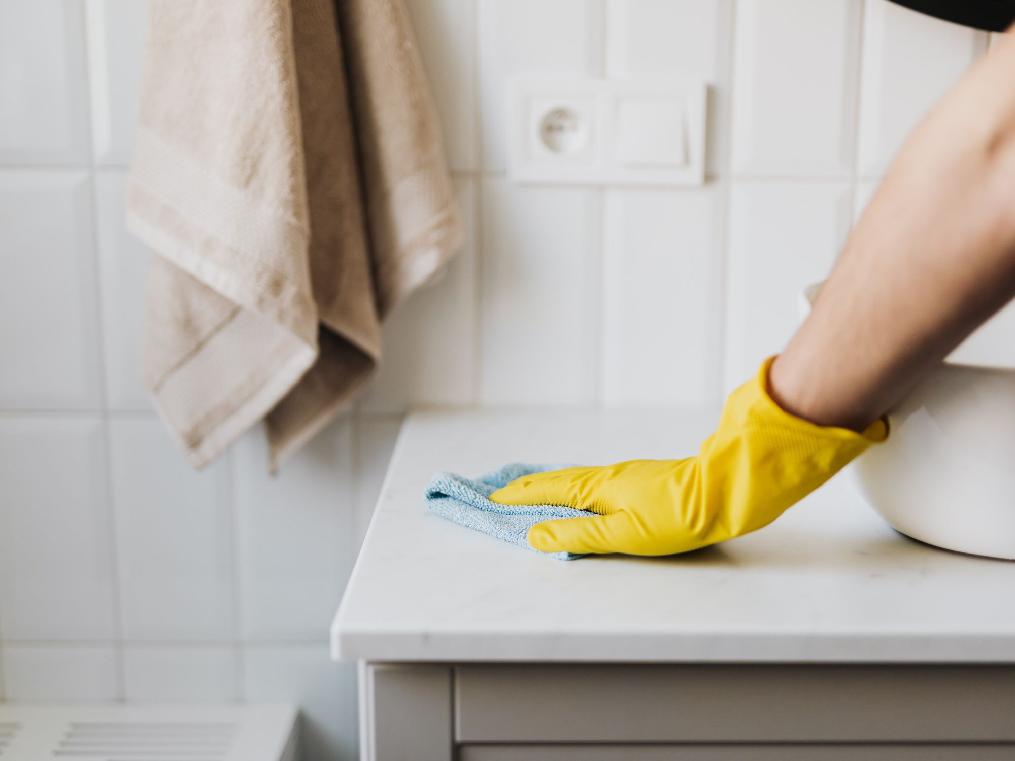 A hand in a yellow glove cleans the surface near a sink