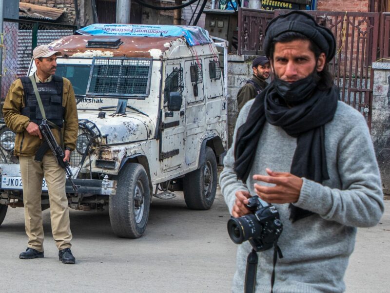 A Kashmiri photojournalist walks past Indian policemen standing on guard outside the closed Kashmir's Grand Mosque or Jamia Masjid.