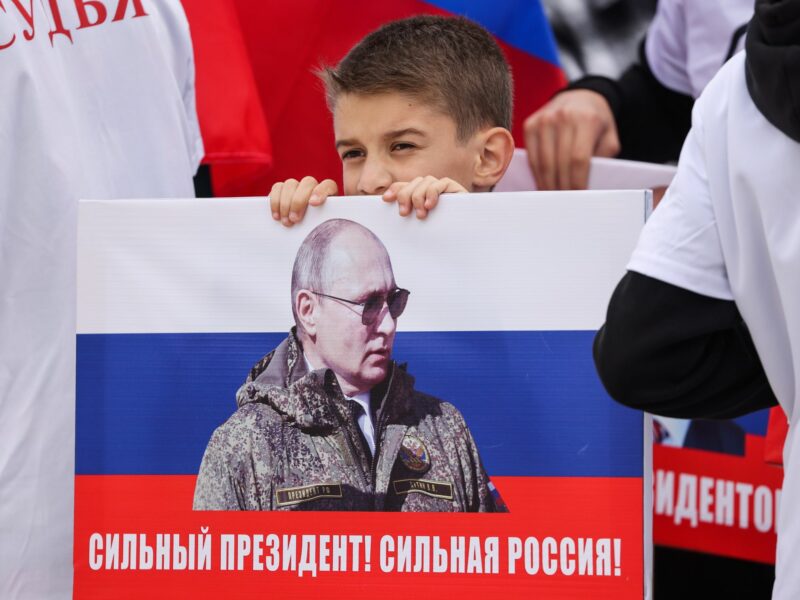 A kid holds up a sign with Putin's photograph over the Russian flag