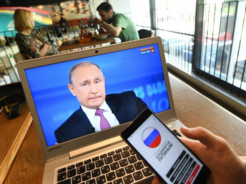 A laptop screen displaying Russian president Vladimir Putin, and phone with his name on it.