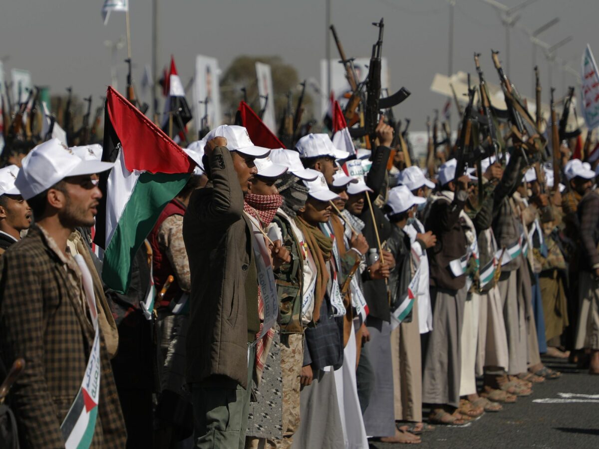 A line of newly recruited Houthi soldiers holding Palestine flags and weapons in the air.