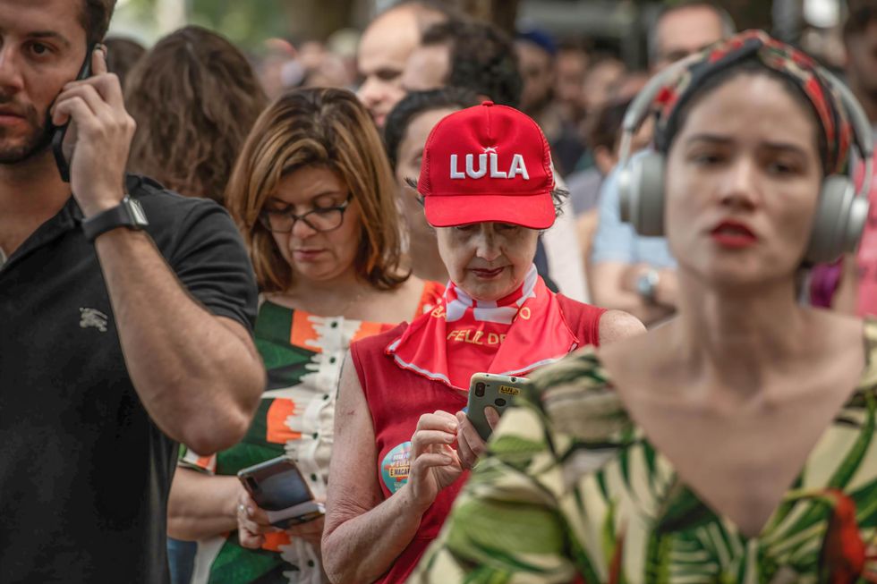 A Lula supporter wearing a red cap and PT scarf looks at her smartphone