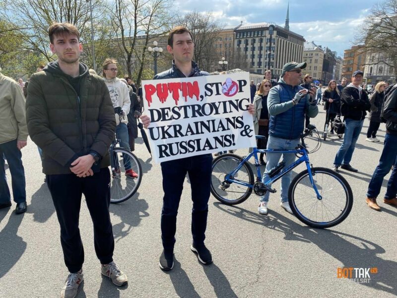 A man holding a "Putin, stop destroying Ukrainians & Russians!" banner.