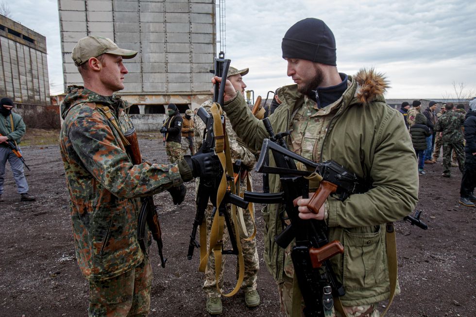 A man in a camouflage uniform collects rifles during a military drill for civilians in the village of Siurte, Zakarpattia Region, western Ukraine.​