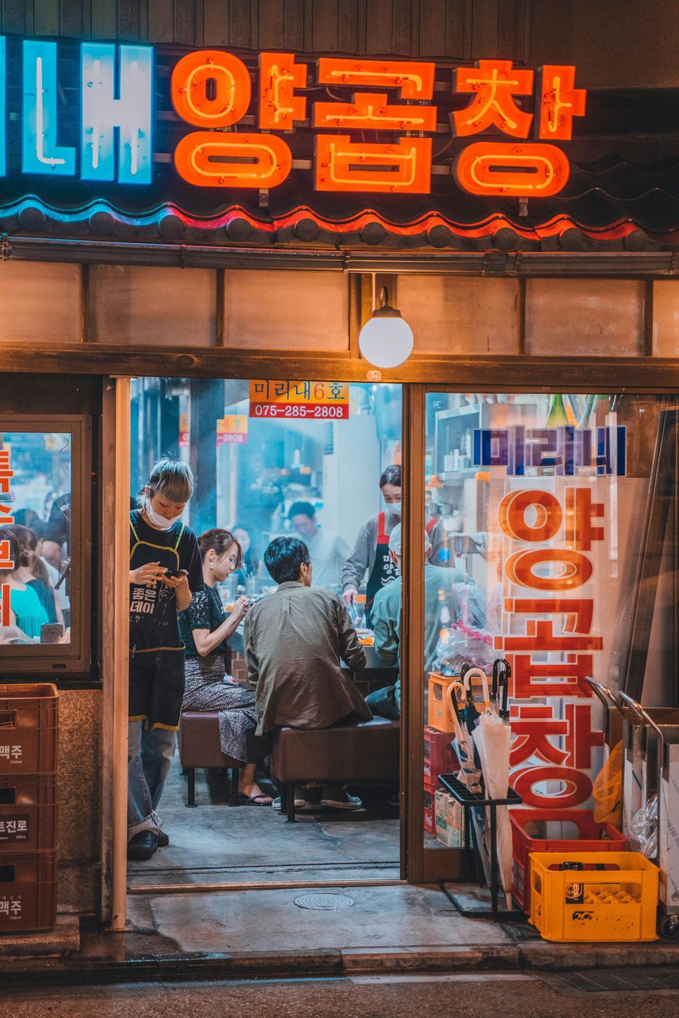 A man in an apron waits at the entrance of a Korean restaurant.
