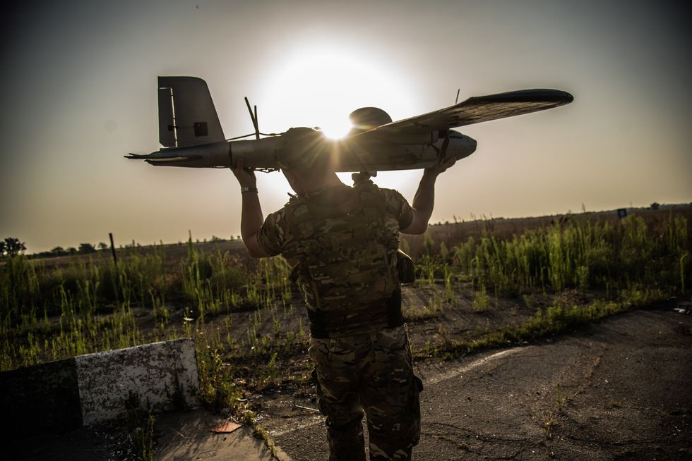 A man in fatigues holds up a drone at head level.