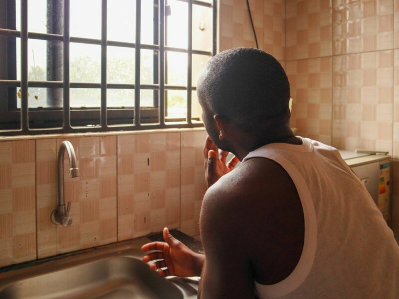A man in Ugandalooks out the window of his kitchen while washing his hands in the sink