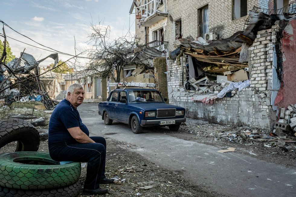 a man is seating on tires as he observes the damages left by a Russian missile strike on a house