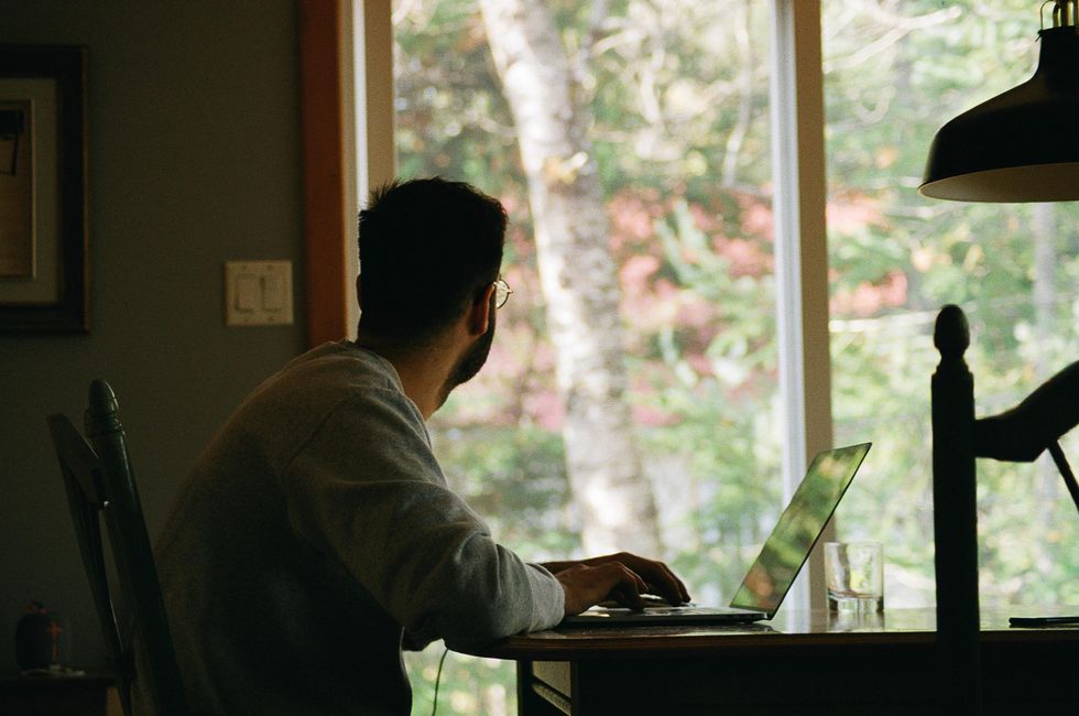 a man looks at his French window while working on his laptop during lockdown