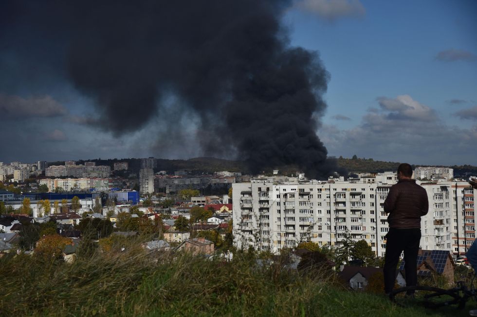 a man standing up a hill watches smoke rising above the buildings after the Russian missile attack on the critical infrastructure of Lviv