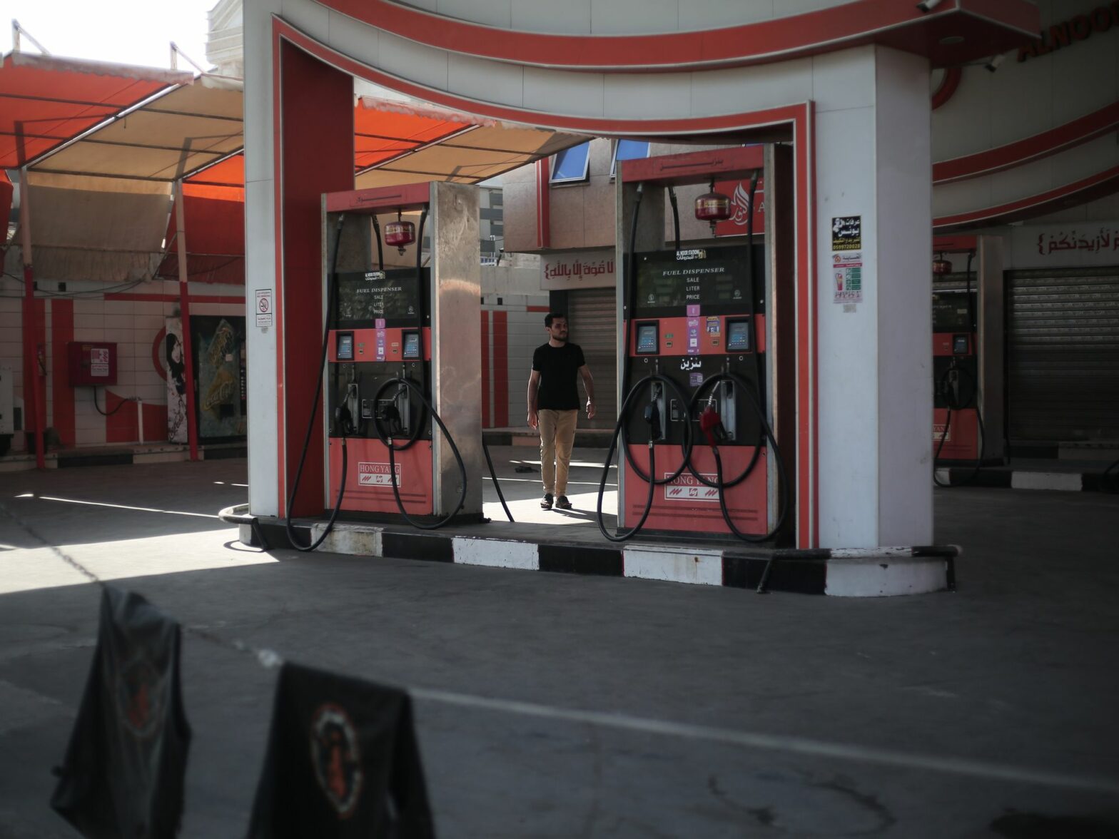 A man stands between two gas pumps at an empty and closed gas station