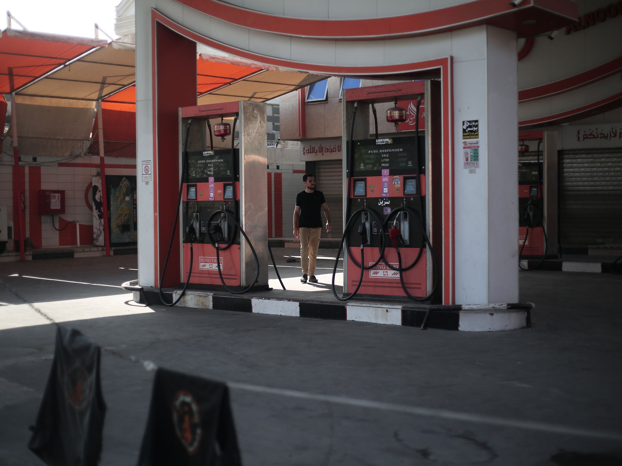 A man stands between two gas pumps at an empty and closed gas station