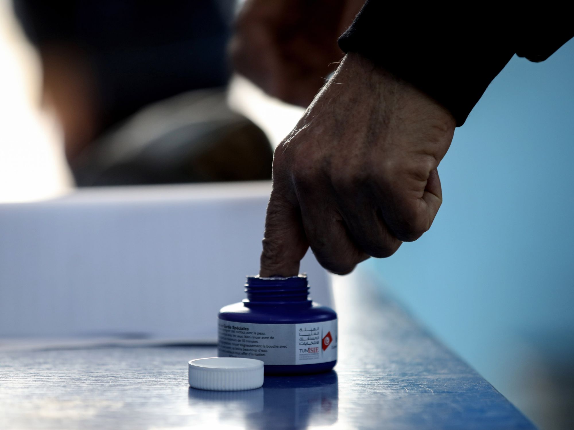 A man sticking his finger in a small container of ink.