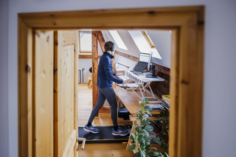 A man takes a call on a headset while walking on a walking pad and working at a desk