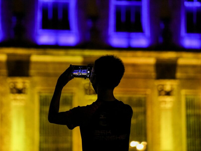 A man takes a picture of the University of Santo Tomas Main Building where the flag of Ukraine is projected in Manila, Philippines