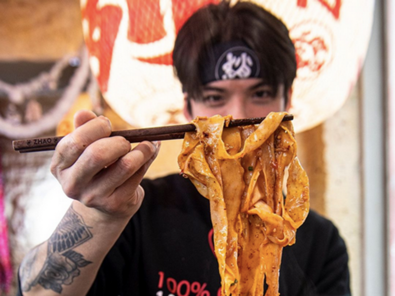 A man uses chopsticks to hold some pasta above a bowl