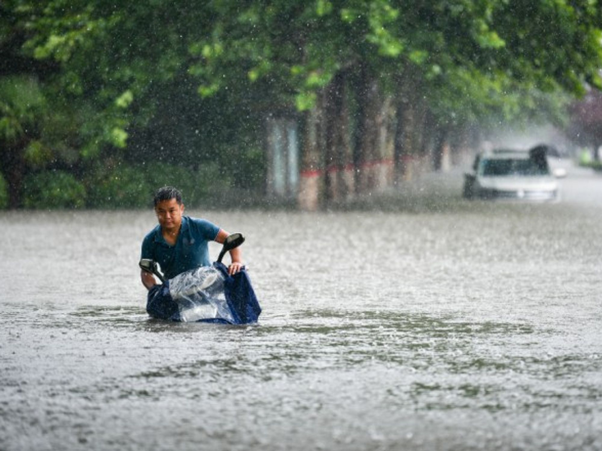 A man wades with his motorbike through Zhengzhou, central China, where thousands were evacuated and a dozens killed following record rains
