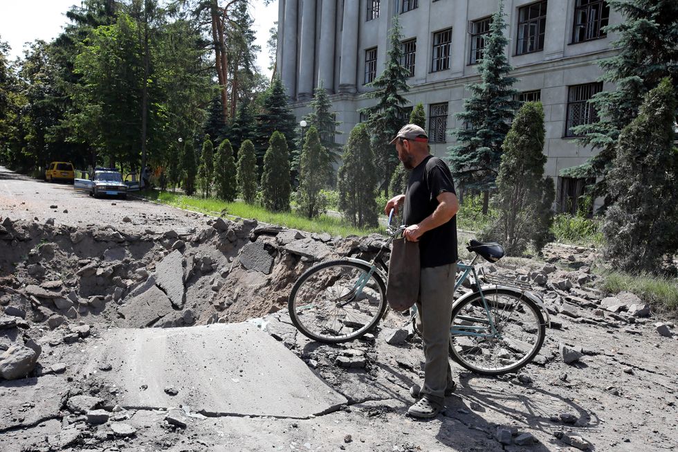 A man walks his bicycle past a huge crater in the street after a Russian rocket hit the Kharkiv region