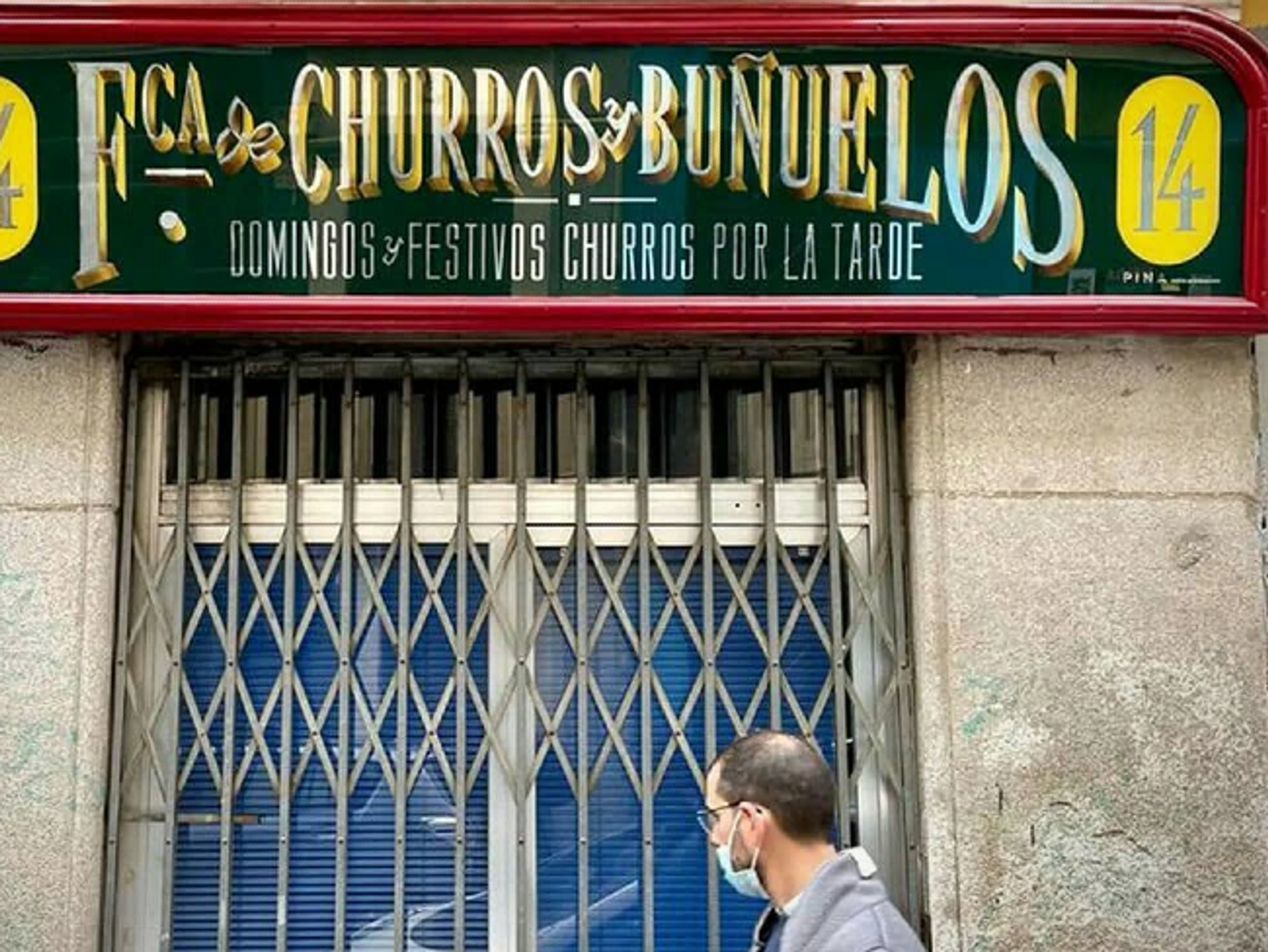 A man walks under a classic spanish shop sign in gold, red and green