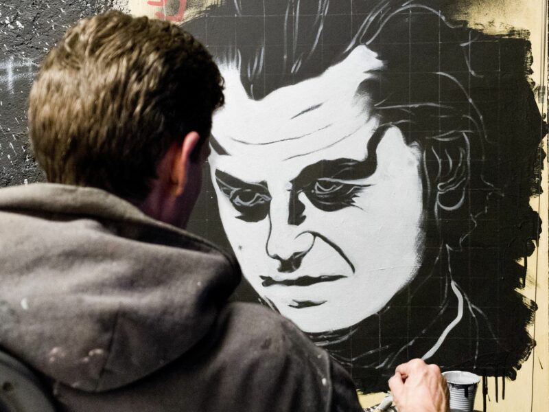 A man with a black hoodie painting a portait of Geert Wilders