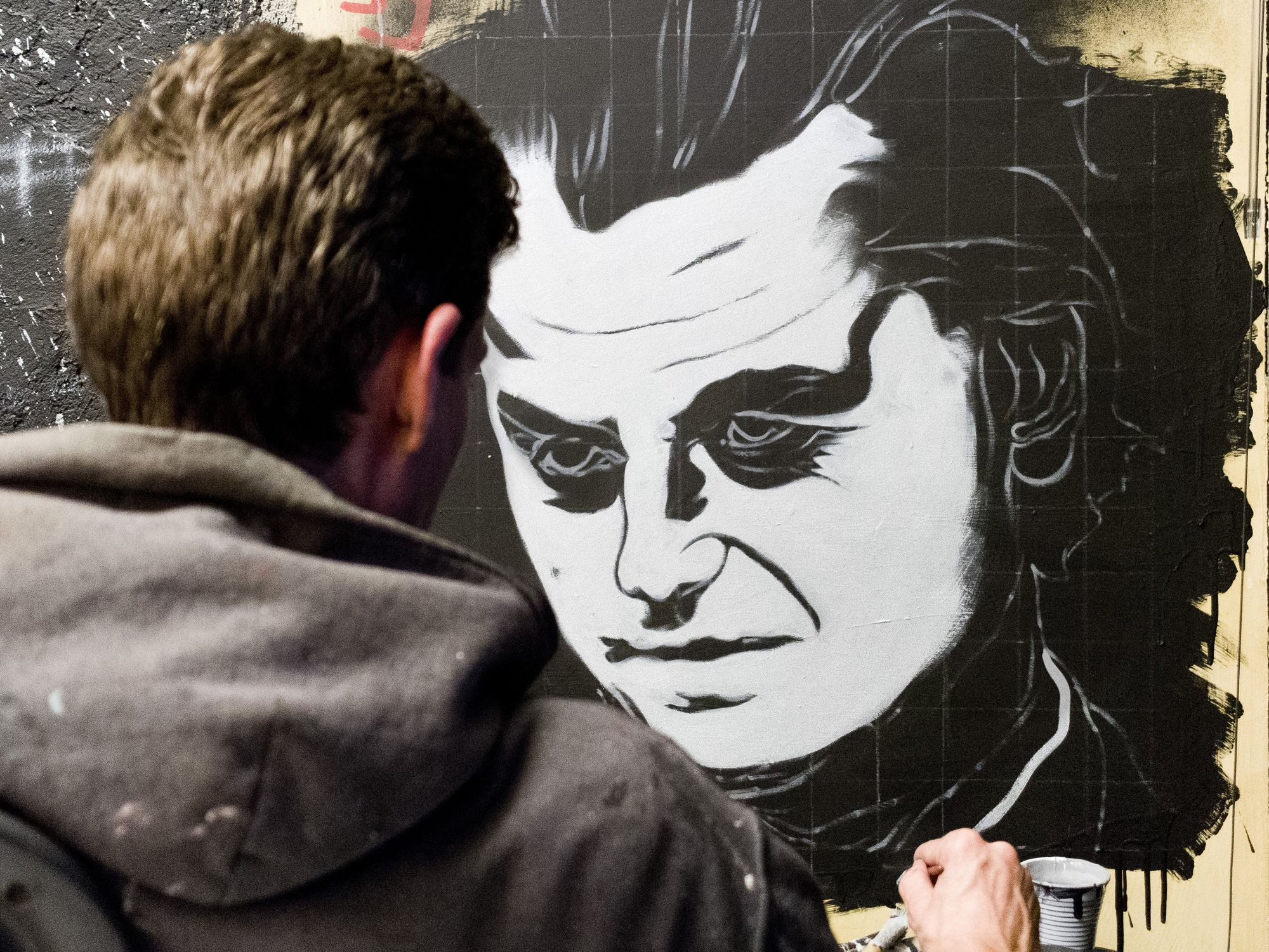 A man with a black hoodie painting a portait of Geert Wilders