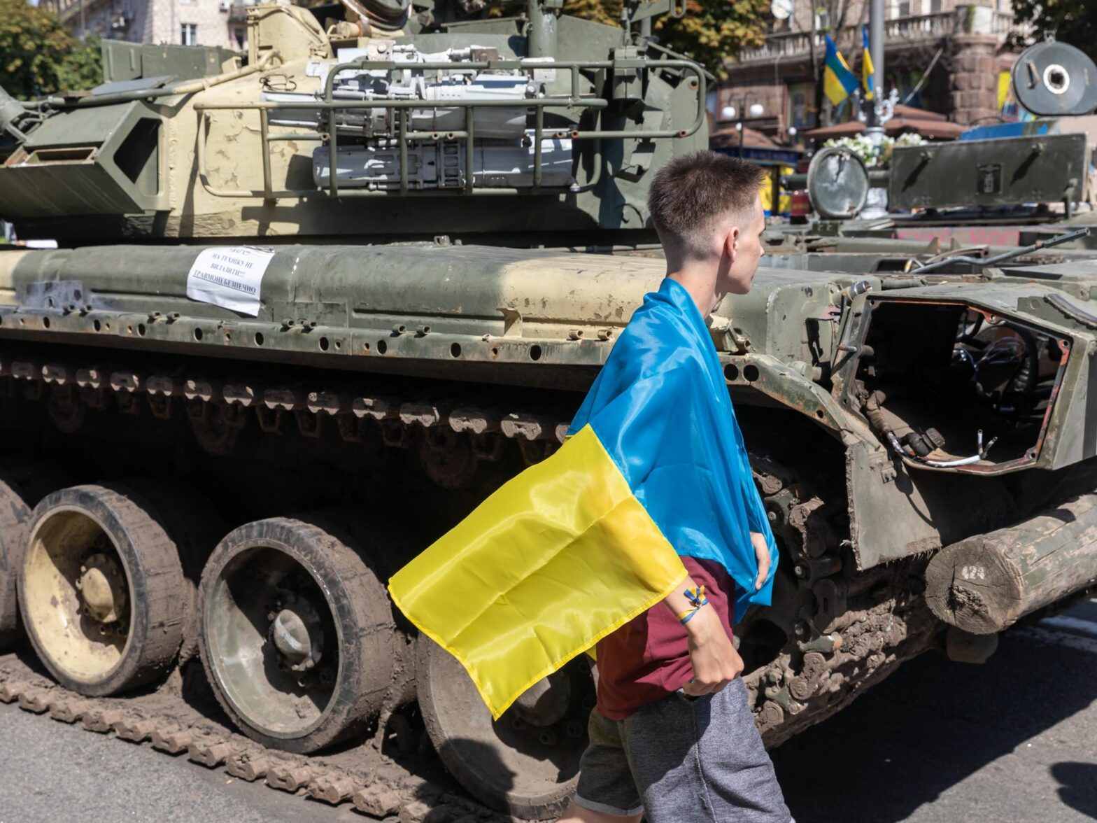 A man wrapped with a Ukrainian flag looks at a destroyed Russian tank at Khreshchatyk, Kyiv