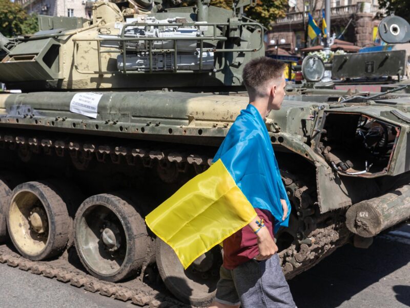 A man wrapped with a Ukrainian flag looks at a destroyed Russian tank at Khreshchatyk, Kyiv