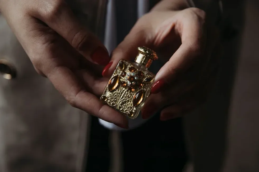 A manicured hand holds a small gold perfume bottle