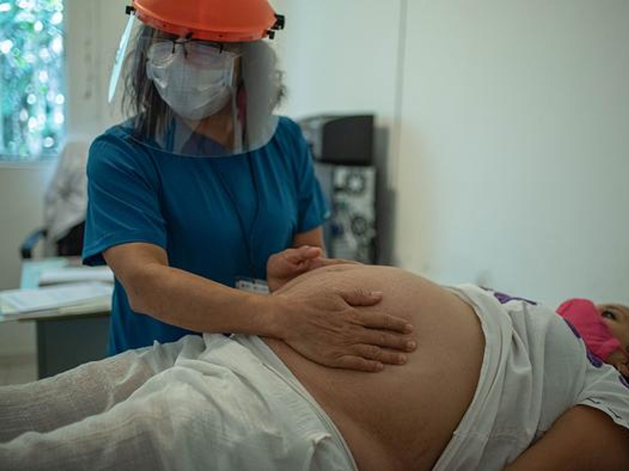 A masked female doctor examining the belly of a pregnant woman for an echographs