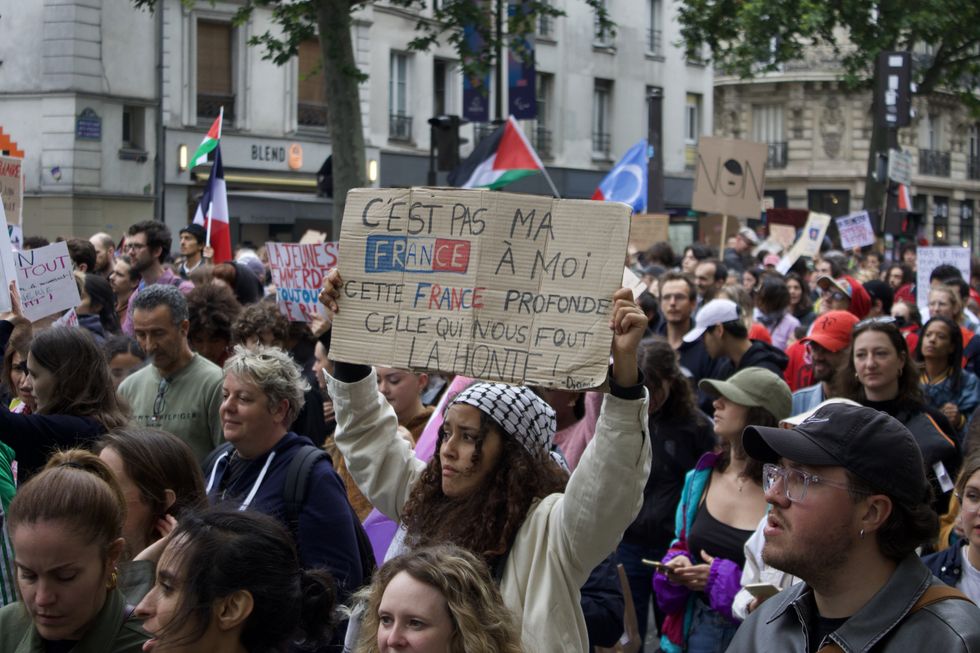 A mass group of protestors with a woman in the center carrying a "C'est pas ma France á moi cette France profonde celle qui nous fout La Honte!" sign.