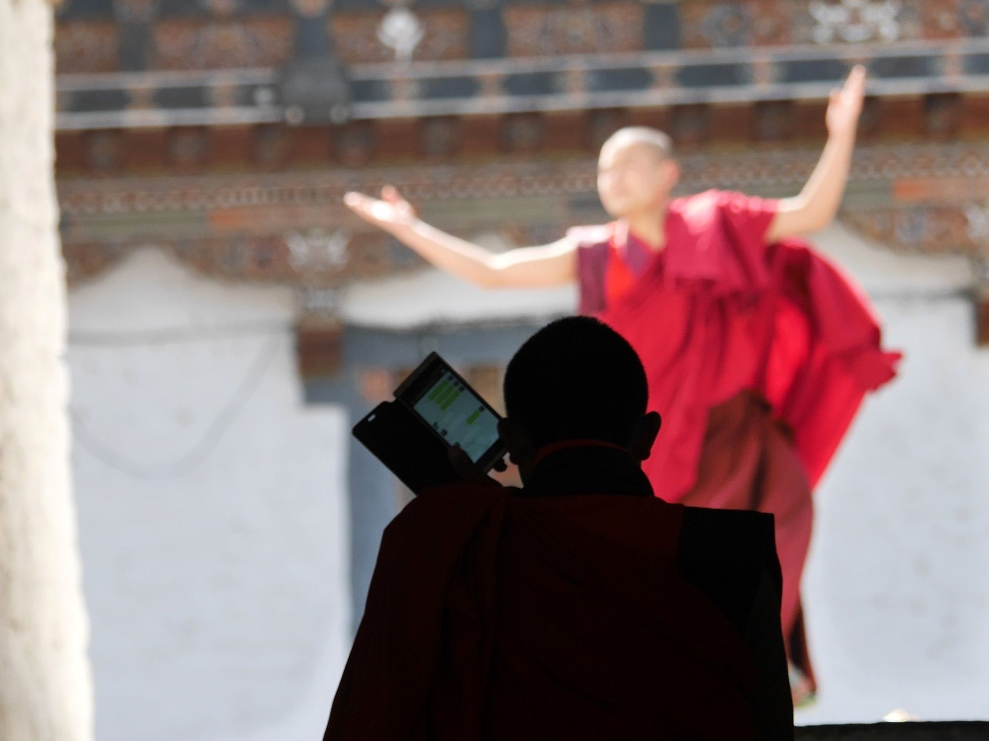 A monk in red performing while a sillouhet of a monk is being illuminated by their phone.