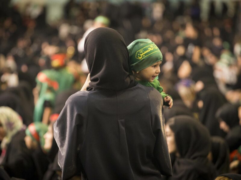 A mother in black with her back turned holding a baby