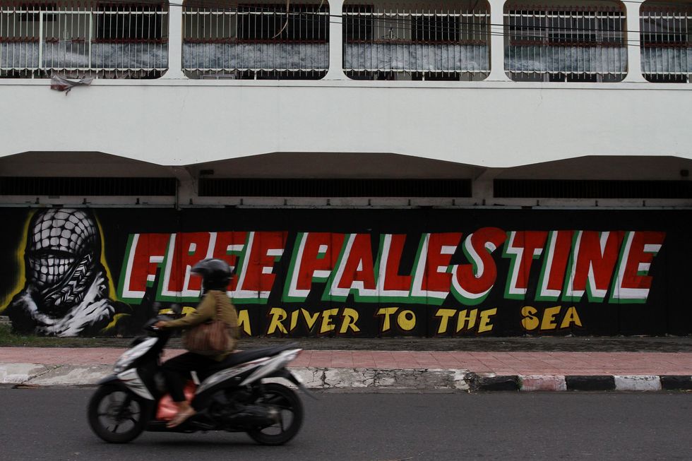 A motorcyclist pass near a mural of support for Palestine on the side of a street in the Yogyakarta city.