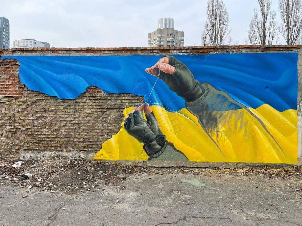 A mural shows hands stitching the Ukrainian flag
