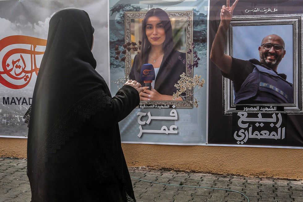 A muslim woman standing in front of two posters of journalists, who were killed the day before in an Israeli strike in south Lebanon.