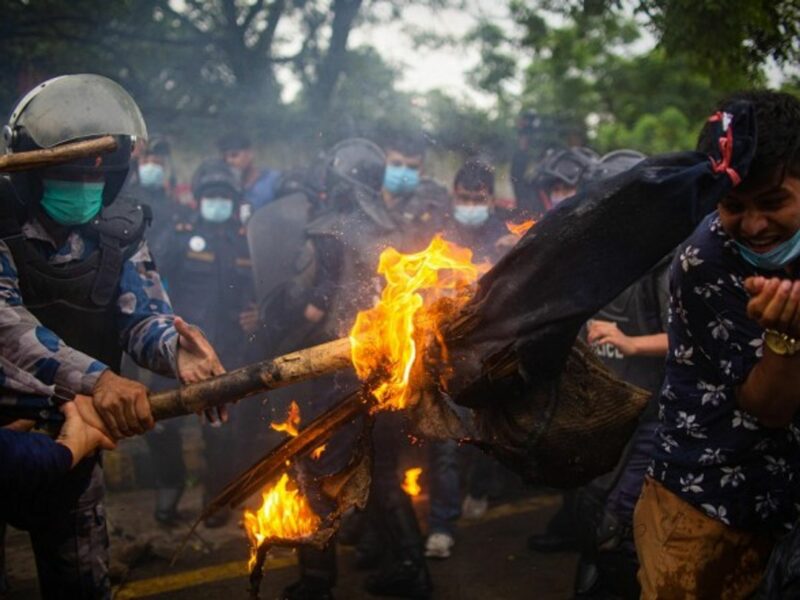 A Nepalese police officer douses burning effigy of PM during a protest in Kathmandu