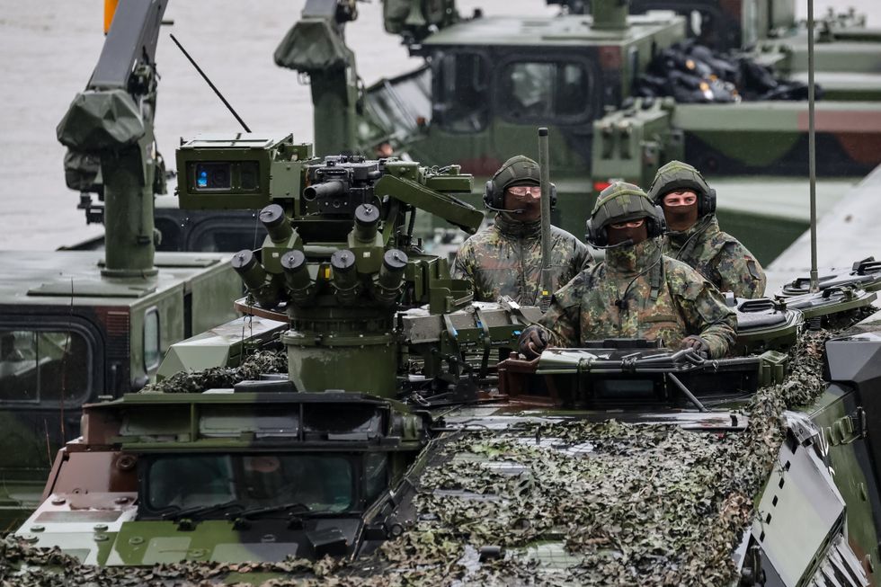 A number of heavy armored vehicles are transferred on boats, with men dressed in camo at the front.