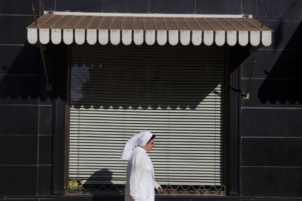A nun passes in front of a closed store in Largo do Camoes, center Lisbon.
