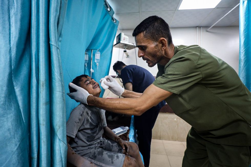 A Palestinan child injured at the hospital while a doctor uses cotton rag to clean him up. We see another doctor in the background working with another patient.