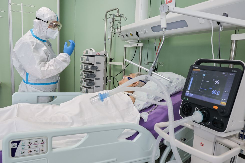 A patient on a hospital bed is connected to a ventilator while a medical worker stands over them.