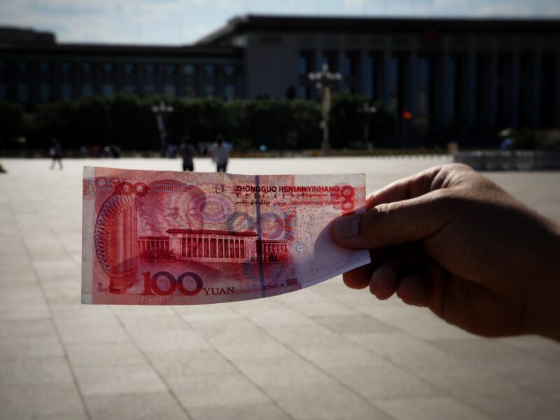 A person holding a 100 yuan bill with a building in the background.