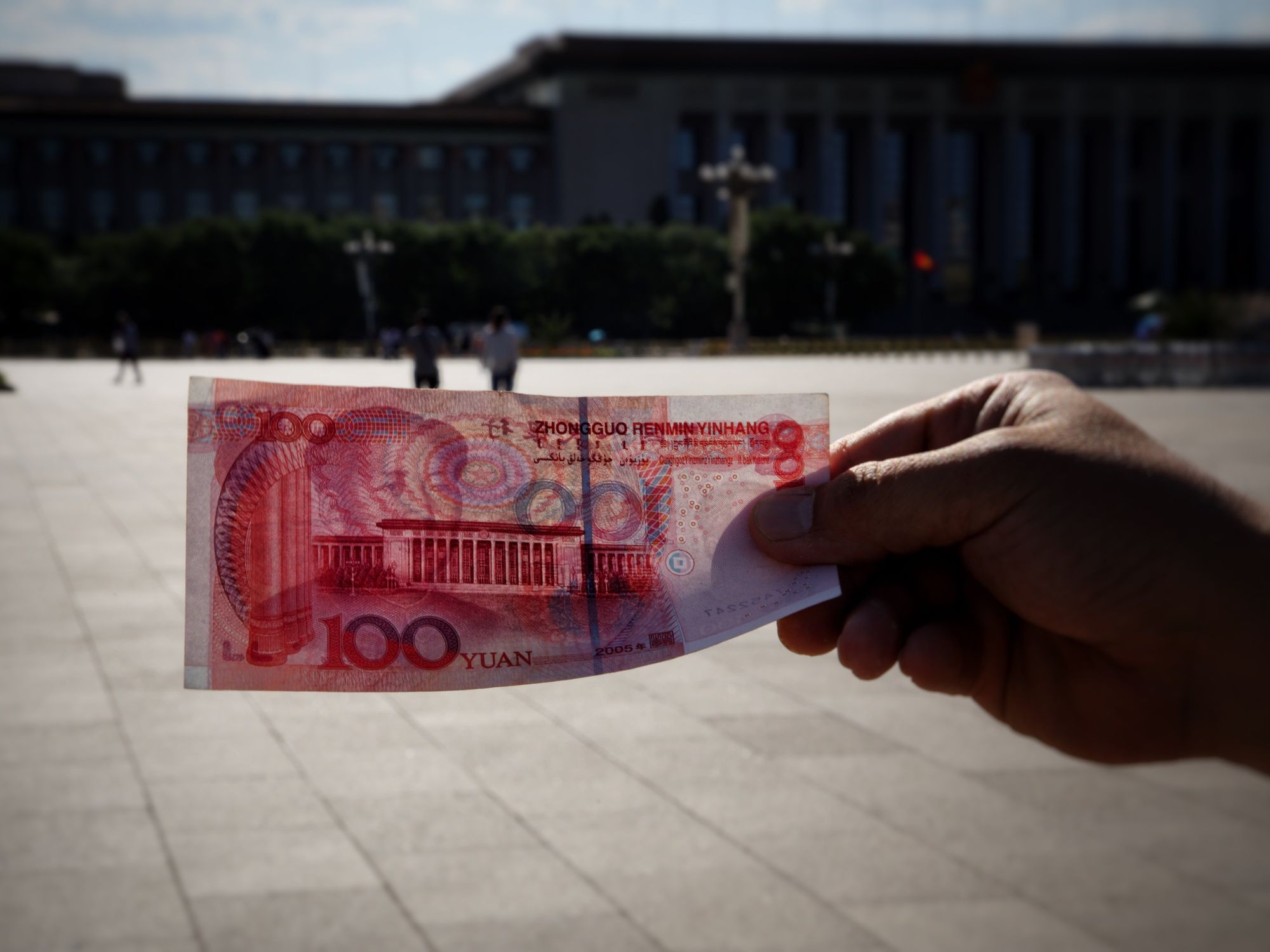 A person holding a 100 yuan bill with a building in the background.