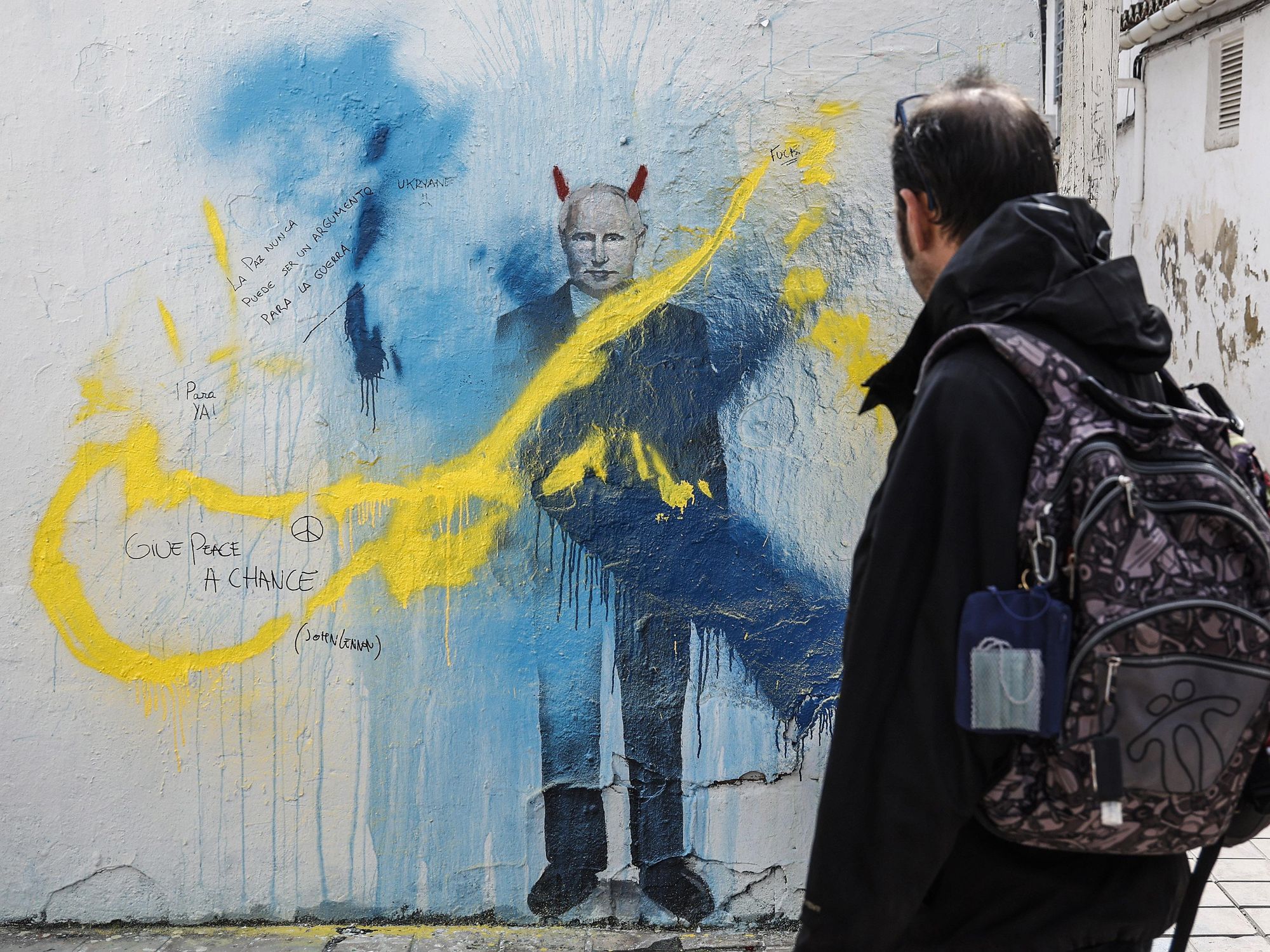 A person observes the graffiti, by Valencian artist J. Warx, with the image of Putin with devil horns and the colors of Ukraine, on a street in Valencia, Spain