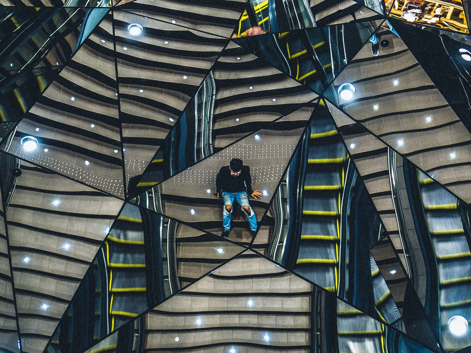 A person wearing ripped jeans and a black long sleeve its in the middle of multiple triangle mirrors.